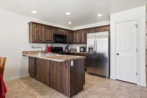 Kitchen with dark wood finish cabinetry, a peninsula, black appliances, light tile patterned flooring, and recessed lighting