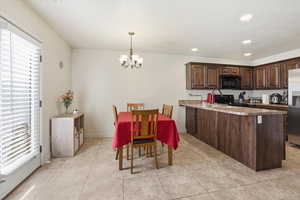 Kitchen featuring a peninsula, dark wood finish cabinetry, black appliances, suspended lighting, and light tile patterned floors