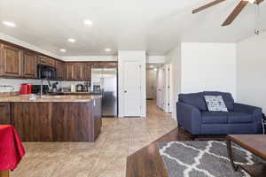Kitchen with dark wood finish cabinets, light tile patterned floors, stainless steel fridge, light countertops, and black microwave
