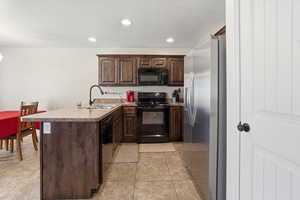 Kitchen with a peninsula, dark wood finish cabinetry, black appliances, recessed lighting, and light countertops