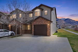 View of front facade with stone siding, a mountain view, concrete driveway, a front lawn, and a garage