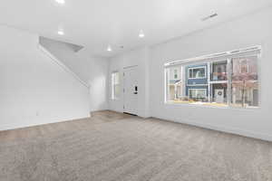 Foyer entrance with healthy amount of natural light, light carpet, and recessed lighting