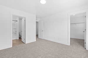 Unfurnished bedroom with a walk in closet, light carpet, and ensuite bathroom