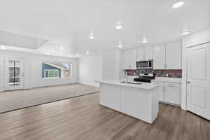 Kitchen featuring white cabinets, stainless steel appliances, an island with sink, open floor plan, and recessed lighting