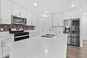 Kitchen featuring white cabinetry, stainless steel appliances, a center island with sink, light stone countertops, and recessed lighting