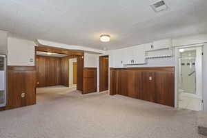 Kitchen featuring wallpapered walls, wainscoting, light colored carpet, open shelves, and white cabinetry