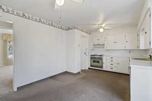 Kitchen with a ceiling fan, light countertops, dark carpet, and white cabinets