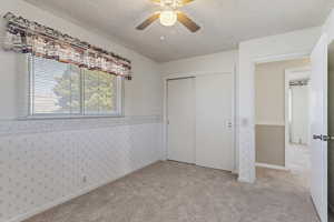 Unfurnished bedroom with a textured ceiling, a closet, light colored carpet, ceiling fan, and wainscoting