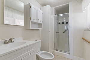 Full bath with vanity, a stall shower, a textured ceiling, and light tile patterned flooring