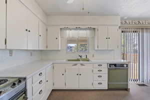 Kitchen featuring light countertops, white cabinets, stainless steel electric stove, a textured ceiling, and dark colored carpet
