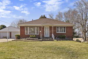 View of front facade with a garage, brick siding, a shingled roof, and an outdoor structure