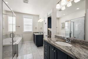 Primary bathroom with a tile shower, two vanities, a garden tub, healthy amount of natural light, and recessed lighting