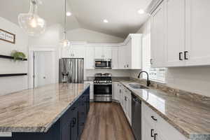 Dual tone kitchen with two tone color scheme, stainless steel appliances, hanging light fixtures, vaulted ceiling, and light stone countertops