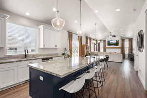 Kitchen with light stone countertops, a kitchen island, two tone color scheme, a kitchen breakfast bar, and dark wood-style flooring