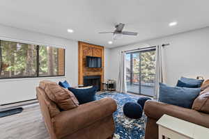 Living room featuring a ceiling fan, a large fireplace, baseboard heating, wood finished floors, and recessed lighting