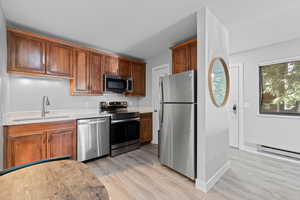 Kitchen featuring stainless steel appliances, light wood-type flooring, wood finish cabinets, and a baseboard radiator