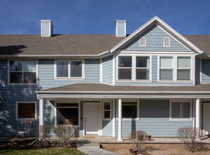 View of front of property featuring a chimney, a porch, and a shingled roof