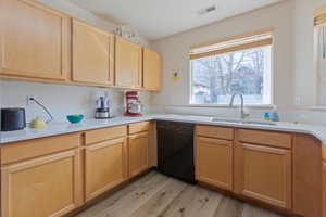 Kitchen with light wood finish cabinetry, black dishwasher, and light wood finished floors