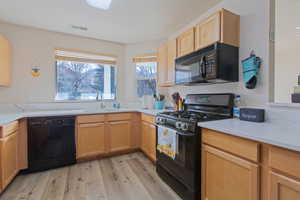 Kitchen featuring black appliances, light wood finish cabinetry, light wood-type flooring, and healthy amount of natural light