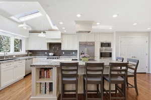 Kitchen featuring built in appliances, a kitchen island, light stone countertops, white cabinets, and light wood-type flooring