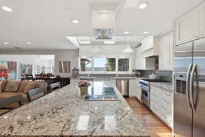 Kitchen with light stone countertops, stainless steel appliances, a kitchen island, white cabinets, and light wood finished floors