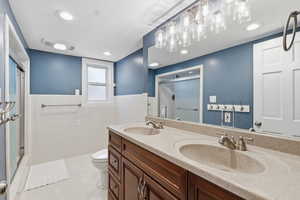Full bathroom featuring double vanity, a shower stall, tile walls, wainscoting, and light tile patterned floors