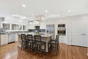 Kitchen featuring light stone counters, stainless steel appliances, a kitchen island, a breakfast bar area, and light wood-style floors
