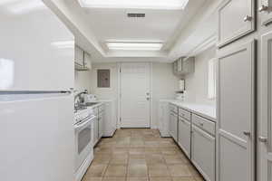 Kitchen featuring white appliances, light countertops, electric panel, light tile patterned floors, and a tray ceiling