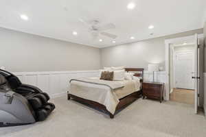 Bedroom with ornamental molding, a wainscoted wall, recessed lighting, a ceiling fan, and light colored carpet