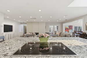 Kitchen with open floor plan, black electric cooktop, light stone countertops, and recessed lighting