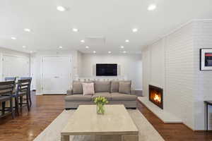 Living area featuring dark wood-type flooring, a brick fireplace, brick wall, and recessed lighting