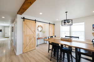Dining area with a barn door, wood walls, light wood-style floors, and hanging lights