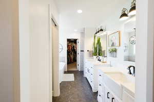 Full bath with a freestanding tub, two vanities, a walk in closet, and recessed lighting
