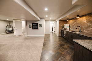Bar area featuring dark wood finish cabinets, light stone counters, brick wall, a textured ceiling, and ceiling fan