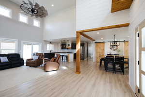 Living area with a barn door, plenty of natural light, light wood-type flooring, a high ceiling, and recessed lighting