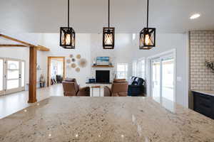 Kitchen featuring light stone countertops, open floor plan, pendant lighting, a fireplace, and wooden walls
