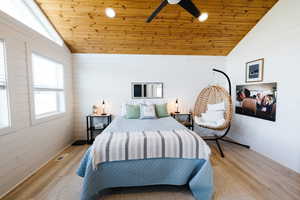 Bedroom featuring a vaulted wood ceiling, wooden walls, light wood-type flooring, and ceiling fan