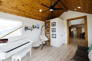 Sitting room featuring light wood-style floors, a wooden ceiling with exposed beams, wood walls, and ceiling fan
