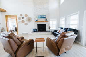 Living room featuring a high ceiling, wooden walls, healthy amount of natural light, a stone fireplace, and wood finished floors