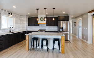 Kitchen featuring light stone counters, stainless steel appliances, backsplash, a kitchen island, and light wood-style floors