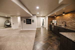 Bar area featuring dark wood finish cabinetry, light stone countertops, a textured ceiling, brick wall, and dark stone finish floors