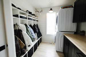 Laundry room with stacked washer / dryer, wooden walls, light wood finished floors, and cabinet space
