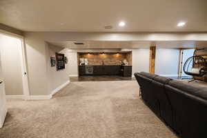 Carpeted living room featuring wet bar, beverage cooler, brick wall, and a textured ceiling