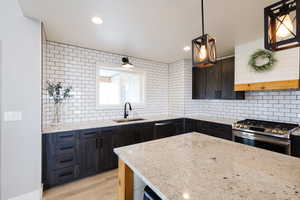 Kitchen featuring backsplash, stainless steel appliances, light stone counters, and light wood finished floors