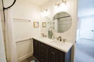 Bathroom featuring double vanity, curtained shower, and dark colored carpet