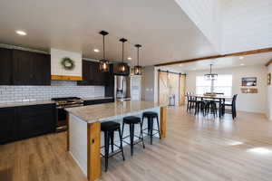 Kitchen with a barn door, stainless steel appliances, decorative light fixtures, and light wood-style floors