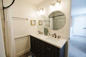 Bathroom with double vanity, a shower with shower curtain, and dark colored carpet