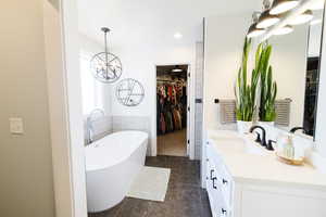 Bathroom with a chandelier, vanity, a soaking tub, a walk in closet, and dark tile patterned flooring