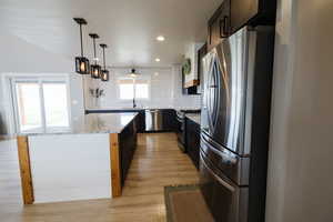 Kitchen with stainless steel appliances, a center island, decorative backsplash, light wood-style flooring, and light stone countertops