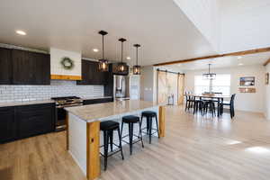 Kitchen featuring a barn door, stainless steel appliances, pendant lighting, and light wood-type flooring